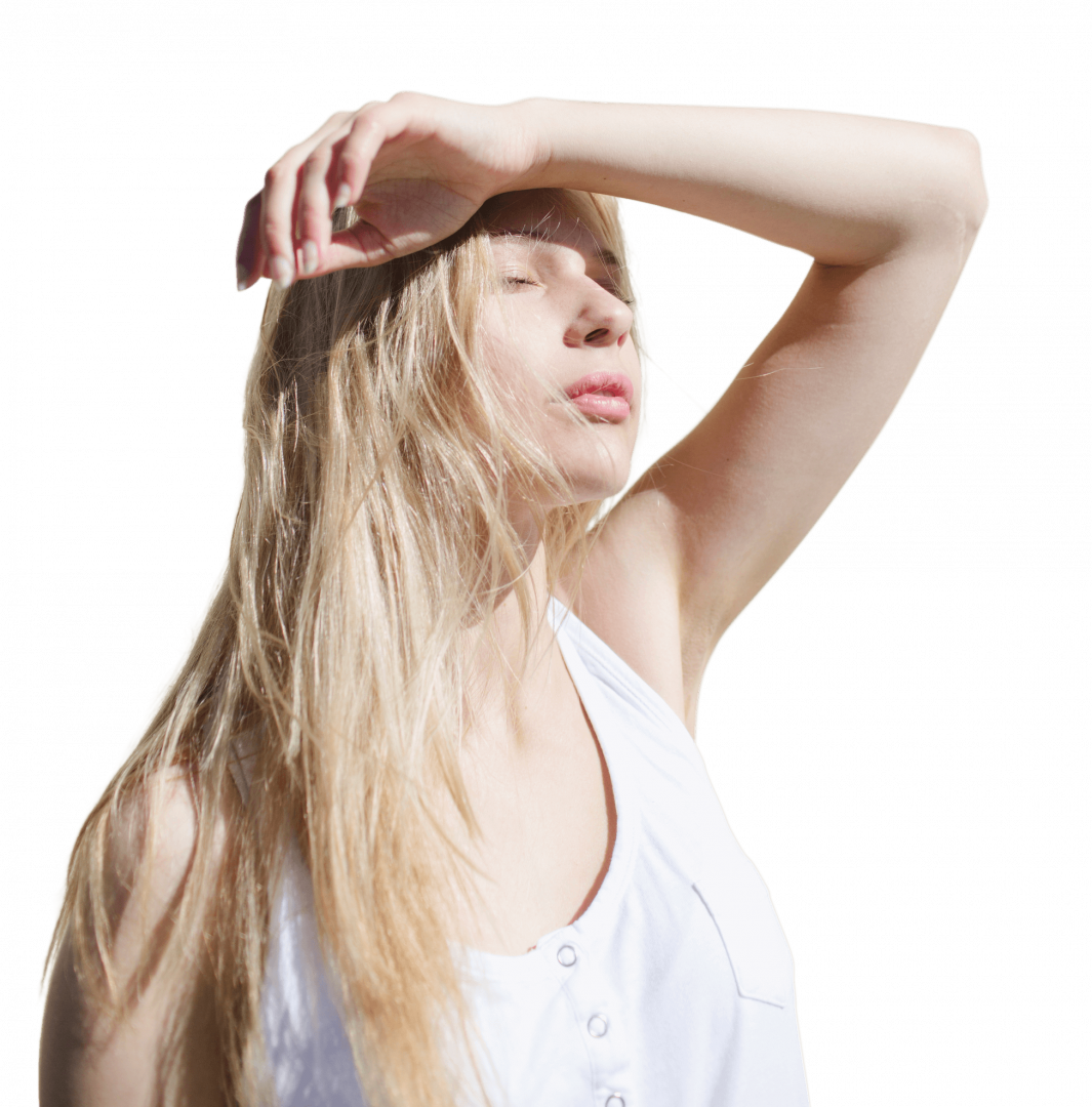 A woman with long blonde hair wearing a white sleeveless top shields her eyes from the bright sunlight with one hand. Her face is angled upwards, basking in the suns warmth as if shes wrapped in the cozy embrace of Merino wool.