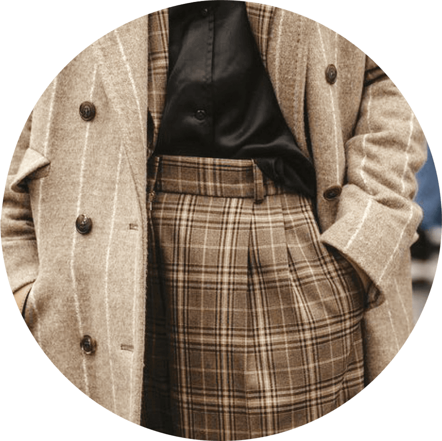 A person is wearing a beige wool coat with vertical stripes over a black shirt. The outfit includes brown plaid high-waisted pants, and the double-breasted Merino coat features dark buttons.