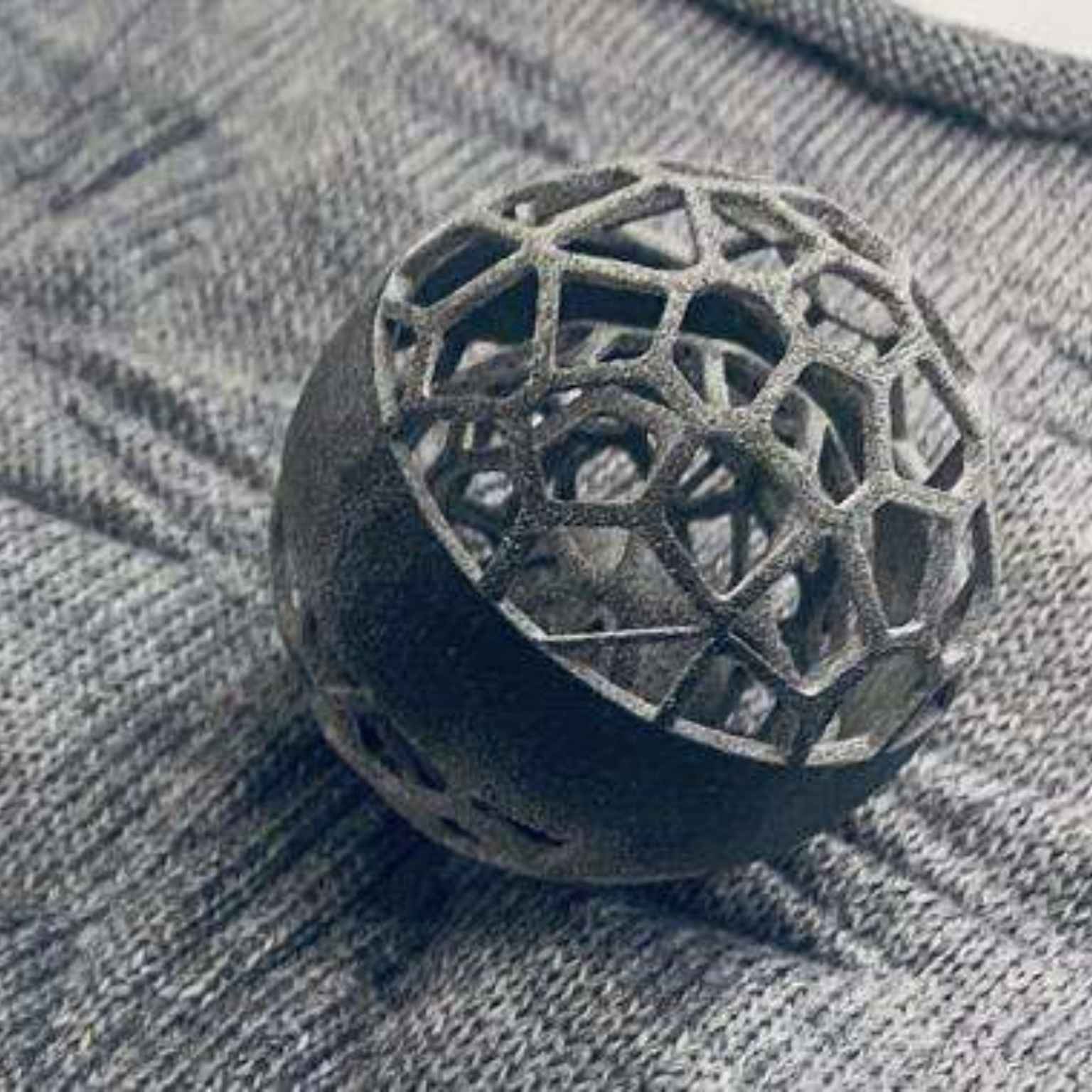 A metal geometric sphere with an open, lattice-like structure sits on a textured gray fabric surface.